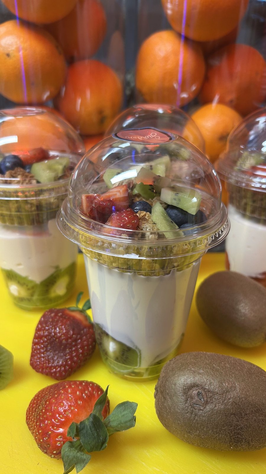 Kubeczki z jogurtem, granolą, kiwi, truskawkami i borówkami na tle pomarańczy